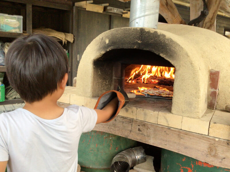 アースオーブンにピザを入れて焼こうとする子ども