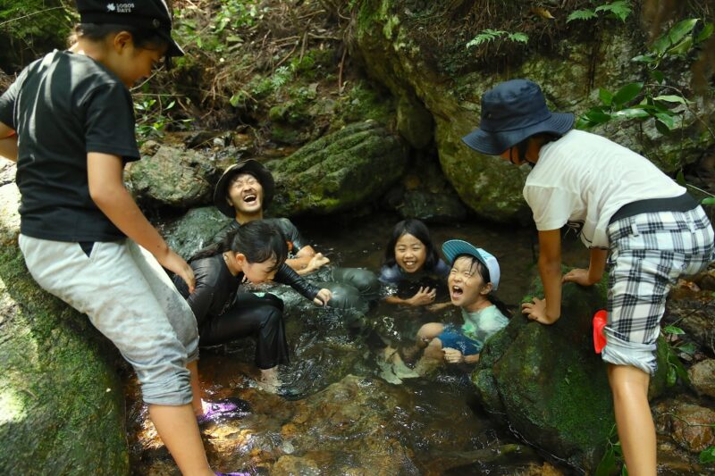 毛鹿洞の沢の深みに座って水に浸かり、水の冷たさに驚き叫ぶ子どもたち