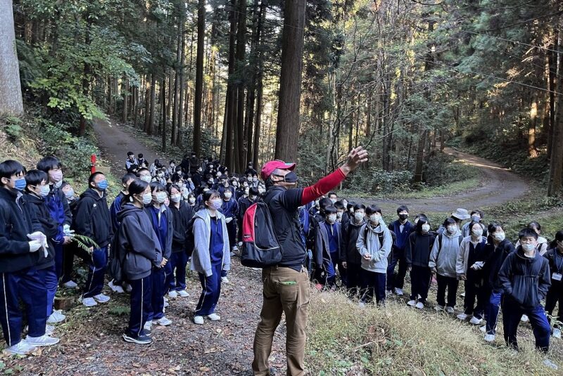 110年生ヒノキ人工林と林業の説明を聞く生徒さん