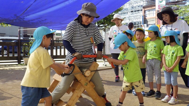 伐採された丸太から円盤を切り出す園児たち