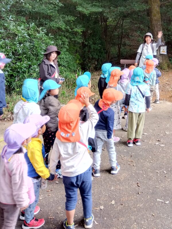 森の入り口で山の動物や危険について説明を受ける園児さん